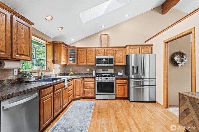 kitchen with a sink, appliances with stainless steel finishes, brown cabinets, and a skylight