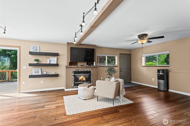 living room featuring track lighting, wood finished floors, a fireplace, baseboards, and a ceiling fan