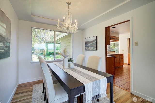 dining area with an inviting chandelier, baseboards, a raised ceiling, and a wealth of natural light
