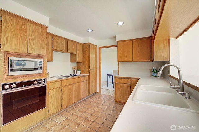 kitchen featuring stovetop with downdraft, a sink, light countertops, stainless steel microwave, and black oven