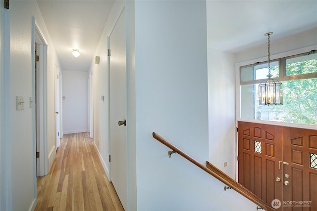 hall featuring a chandelier, baseboards, an upstairs landing, and light wood finished floors