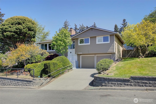split level home featuring a front lawn, fence, a chimney, an attached garage, and driveway