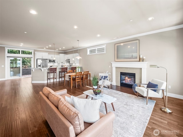 living room featuring crown molding, a tiled fireplace, recessed lighting, baseboards, and dark wood-type flooring