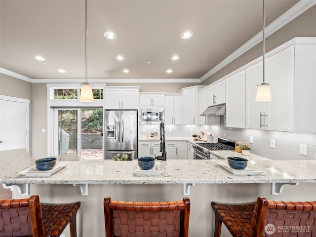 kitchen featuring a peninsula, light stone countertops, a breakfast bar, under cabinet range hood, and appliances with stainless steel finishes