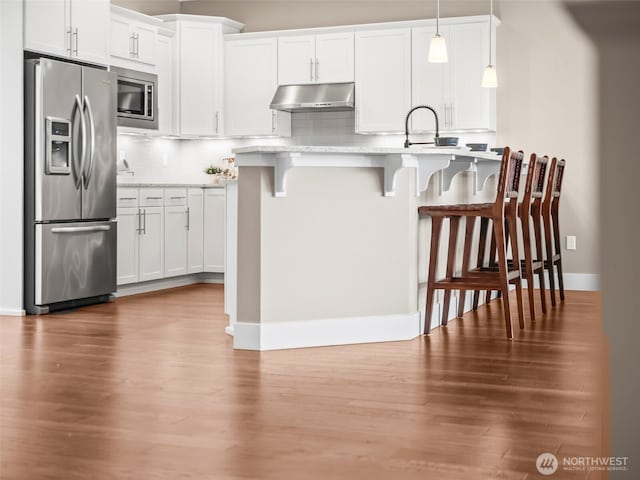 kitchen with wood finished floors, light countertops, under cabinet range hood, a breakfast bar, and stainless steel appliances