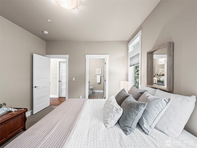 bedroom with ensuite bathroom, baseboards, and dark carpet