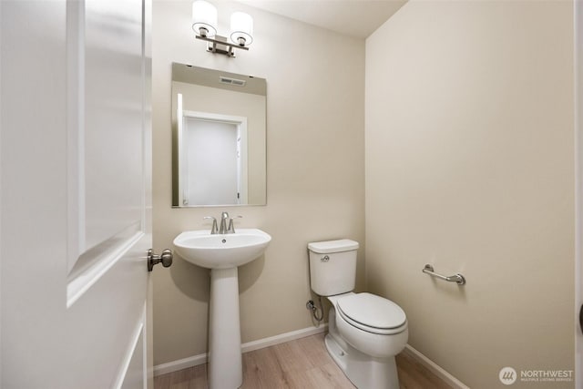 half bath with visible vents, wood finished floors, a sink, baseboards, and toilet