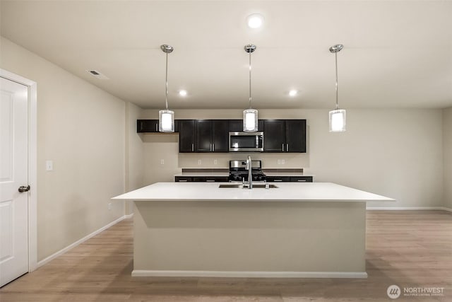 kitchen featuring light countertops, stainless steel appliances, a kitchen island with sink, and light wood finished floors