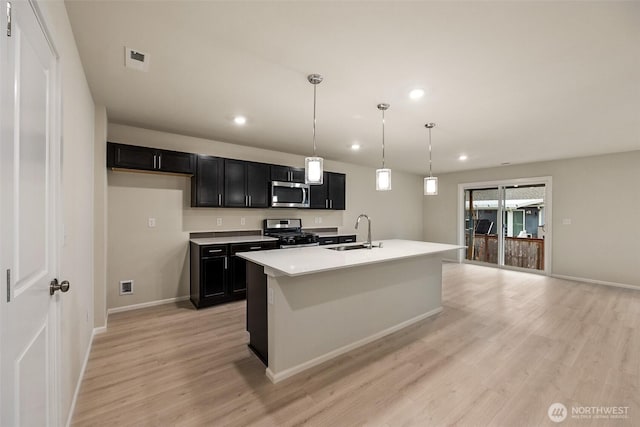 kitchen with appliances with stainless steel finishes, a sink, light wood-style floors, dark cabinetry, and recessed lighting