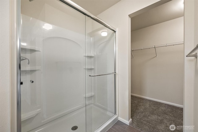 full bath with baseboards, a walk in closet, and a stall shower