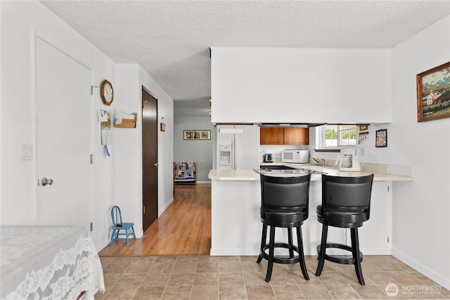 109 Lime St, Omak, WA 98841 - kitchen with white appliances, light countertops, a textured ceiling, brown cabinetry, and a peninsula