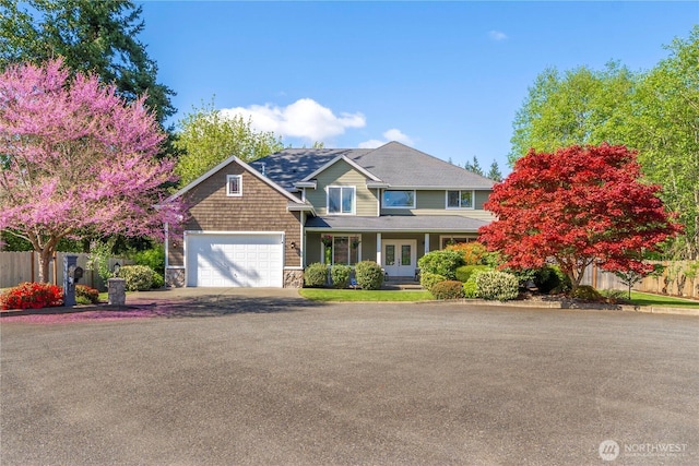 view of front of property with fence, an attached garage, stone siding, french doors, and driveway