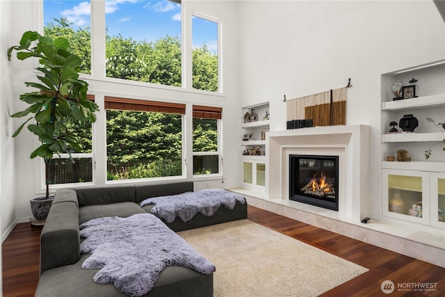 living room featuring a high end fireplace, built in shelves, wood finished floors, and a towering ceiling
