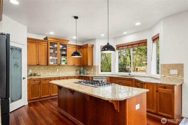 kitchen featuring stainless steel gas cooktop, dark wood-style floors, brown cabinetry, and a kitchen island