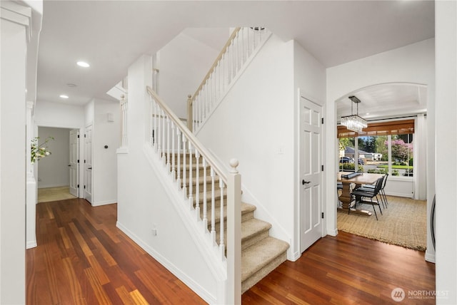 stairs with arched walkways, baseboards, recessed lighting, and wood finished floors
