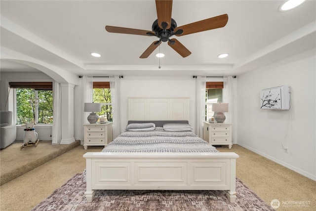 bedroom with light colored carpet, arched walkways, baseboards, and a tray ceiling