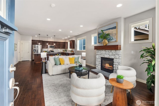 living area with recessed lighting, baseboards, dark wood-style floors, and a stone fireplace