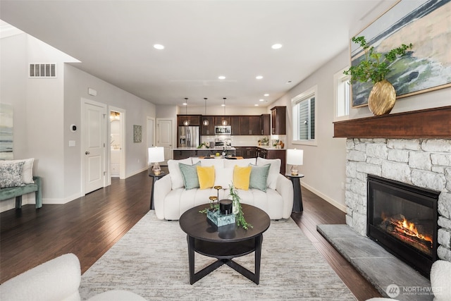 living area featuring baseboards, a fireplace, dark wood-style flooring, and visible vents