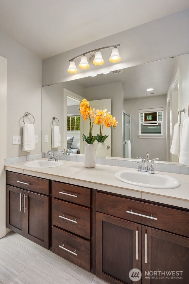 full bathroom with a sink, a shower with door, double vanity, and visible vents