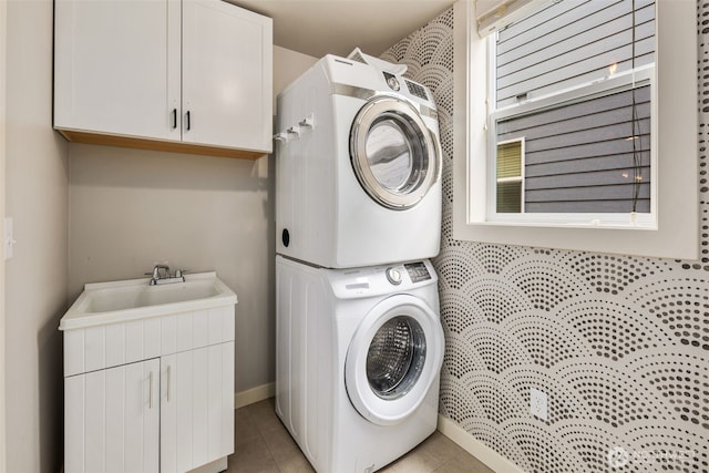 clothes washing area with a sink, cabinet space, light tile patterned floors, and stacked washer / dryer
