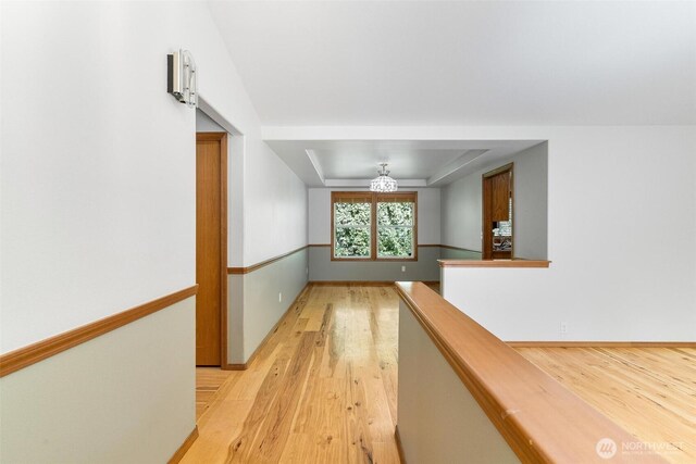 hall featuring light wood-style floors, a raised ceiling, and baseboards