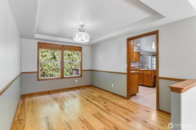 empty room with a raised ceiling, baseboards, light wood finished floors, and a chandelier