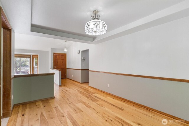 unfurnished room featuring a tray ceiling, an inviting chandelier, baseboards, and light wood finished floors