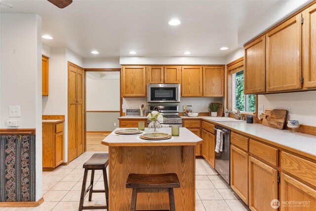 kitchen with appliances with stainless steel finishes, a breakfast bar, a sink, light countertops, and a center island