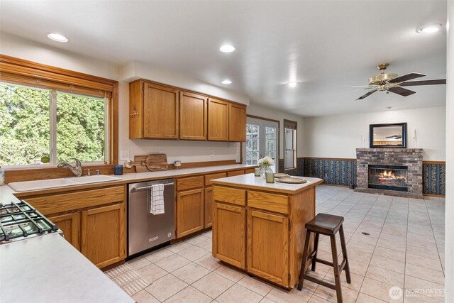 kitchen featuring light tile patterned flooring, wainscoting, a sink, light countertops, and stainless steel dishwasher