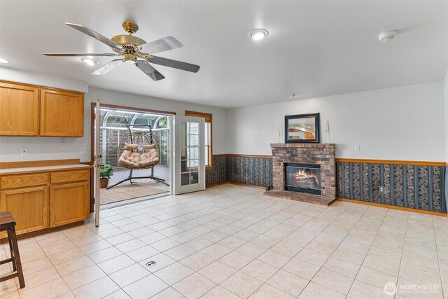 unfurnished living room with a ceiling fan, wainscoting, a brick fireplace, light tile patterned floors, and recessed lighting