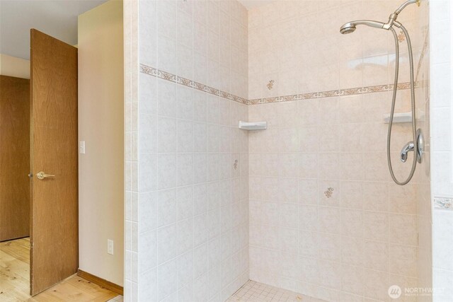 full bath featuring wood finished floors and a tile shower