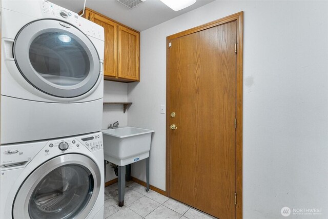 laundry room featuring cabinet space, light tile patterned flooring, stacked washing maching and dryer, baseboards, and visible vents