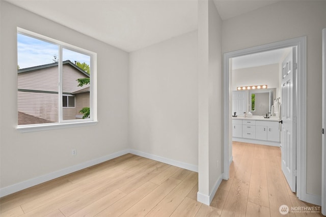 unfurnished bedroom featuring light wood-style floors, connected bathroom, and baseboards
