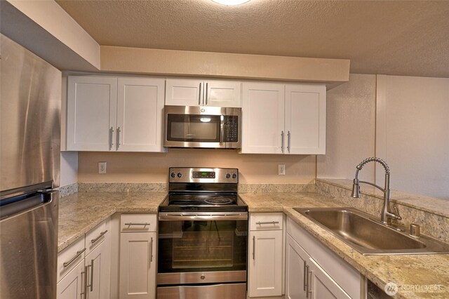 kitchen with white cabinets, stainless steel appliances, a textured ceiling, and a sink