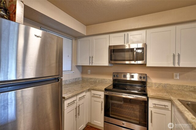 kitchen featuring light stone counters, a textured ceiling, white cabinets, and stainless steel appliances