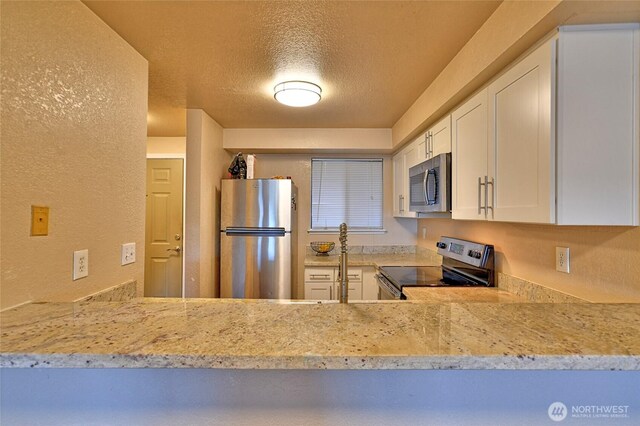 kitchen featuring a textured ceiling, light stone countertops, white cabinets, a textured wall, and stainless steel appliances