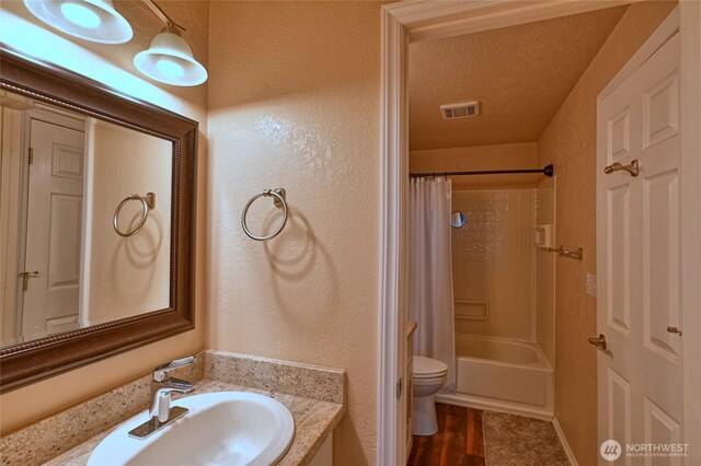 bathroom featuring a textured wall, vanity, toilet, shower / tub combo, and visible vents