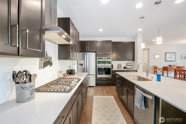 kitchen featuring wood finished floors, light countertops, a sink, appliances with stainless steel finishes, and hanging light fixtures
