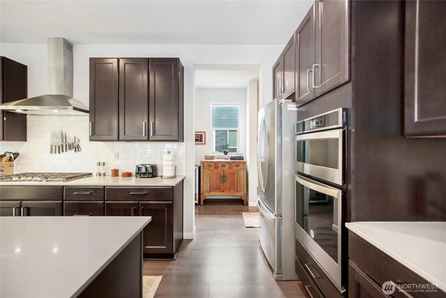 kitchen featuring light countertops, appliances with stainless steel finishes, dark brown cabinets, and wall chimney range hood