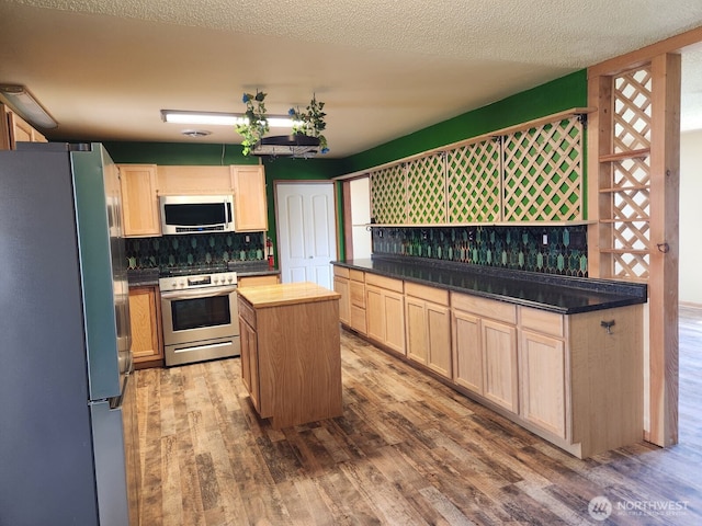 kitchen with decorative backsplash, a center island, wood finished floors, light brown cabinets, and stainless steel appliances