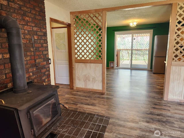 doorway to outside with a textured ceiling, dark wood finished floors, a wood stove, and brick wall