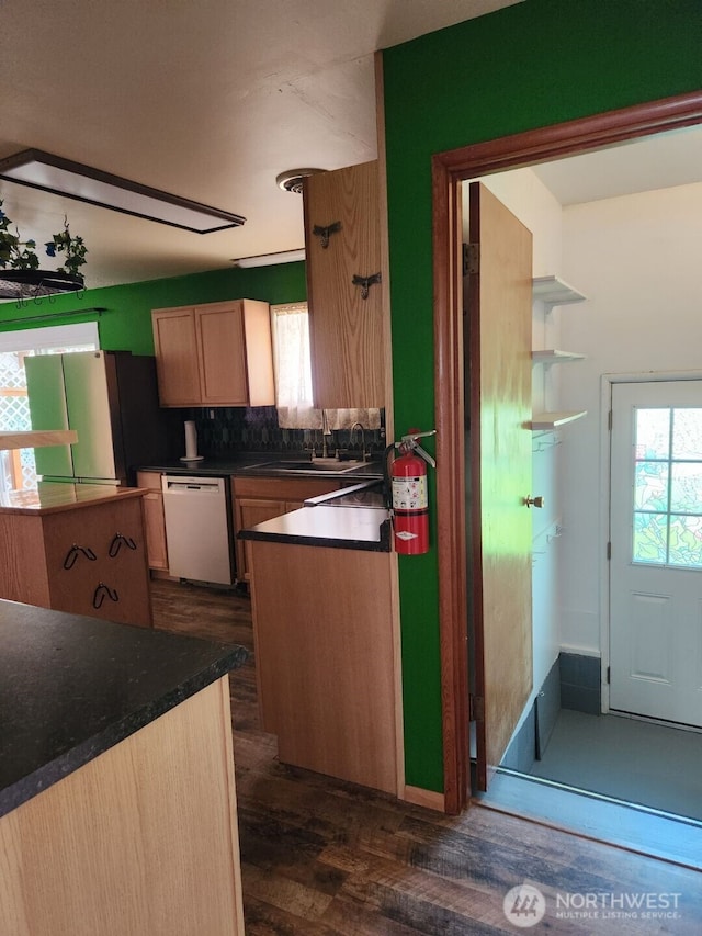 kitchen featuring dark countertops, dishwasher, freestanding refrigerator, backsplash, and dark wood-style floors