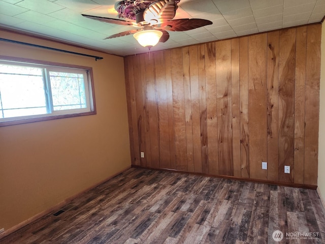 empty room with visible vents, ceiling fan, wooden walls, and dark wood-style floors