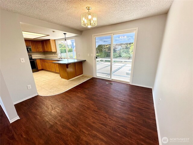 kitchen with brown cabinetry, a peninsula, a notable chandelier, stainless steel appliances, and light wood-style flooring