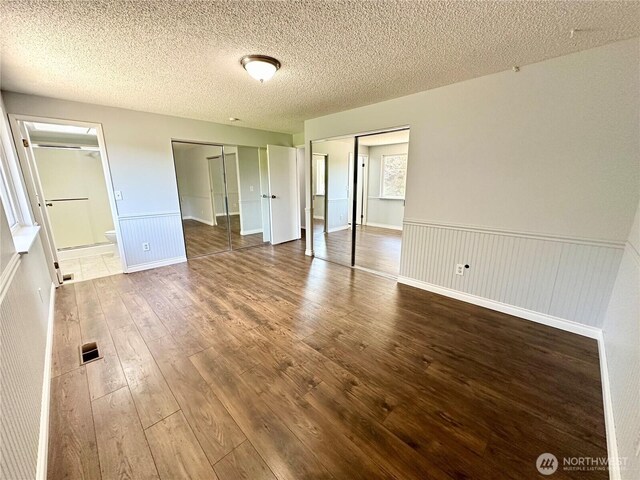 unfurnished bedroom featuring a textured ceiling, visible vents, wainscoting, and hardwood / wood-style floors