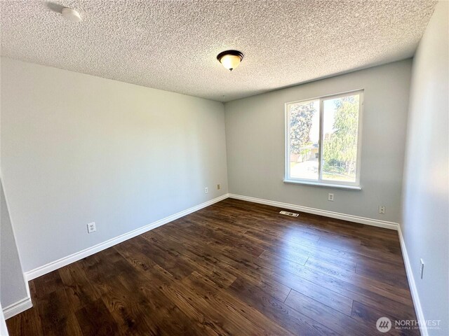 empty room featuring baseboards, visible vents, a textured ceiling, and dark wood-type flooring