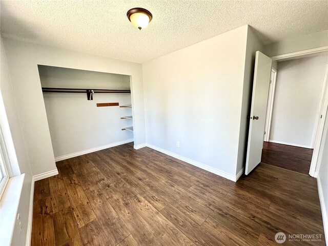 unfurnished bedroom featuring baseboards, a textured ceiling, dark wood-style flooring, and a closet