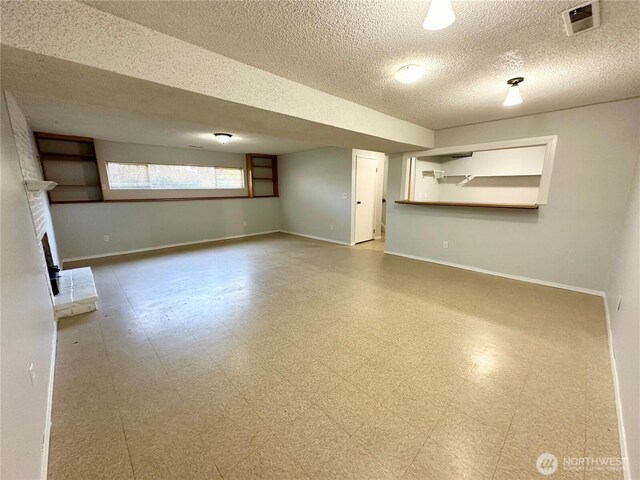 basement with visible vents, a brick fireplace, baseboards, a textured ceiling, and tile patterned floors