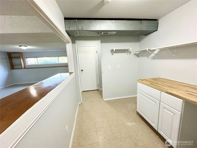 corridor with baseboards, visible vents, and light floors
