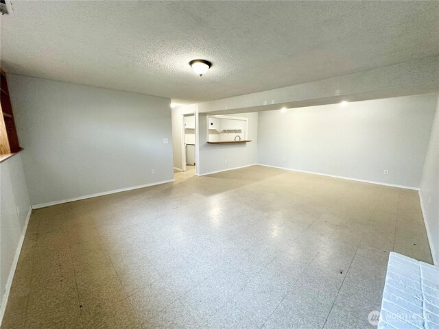 finished below grade area featuring tile patterned floors, baseboards, and a textured ceiling